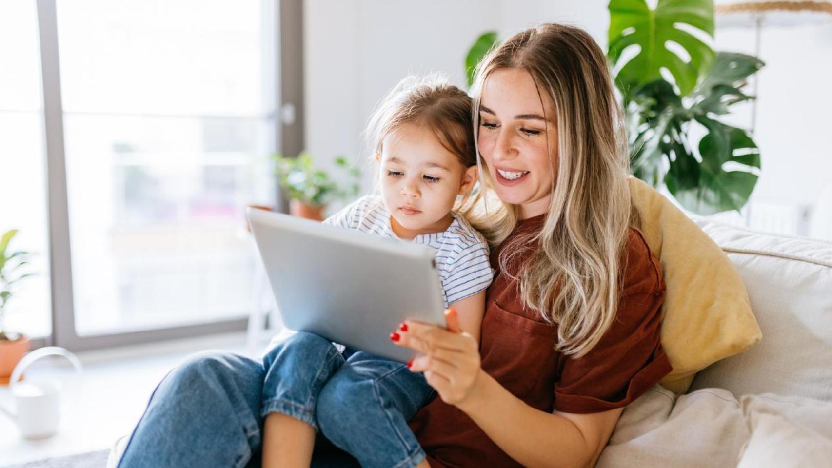 Madre con su hija en brazos mirando una tablet.