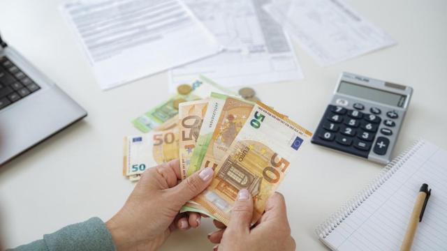 Una mujer contando billetes de euros junto a una calculadora.