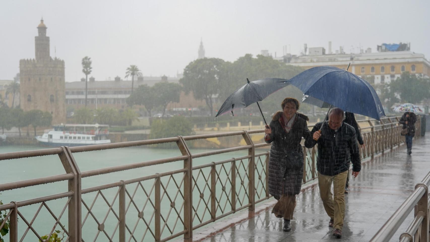 Dos personas se protegen de la lluvia en el Puente de San Telmo de Sevilla.