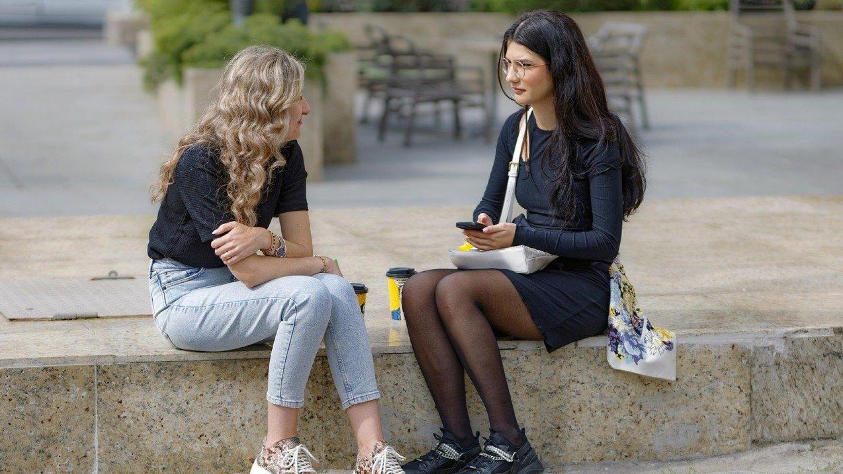 Dos jóvenes hablando sentadas en la calle.