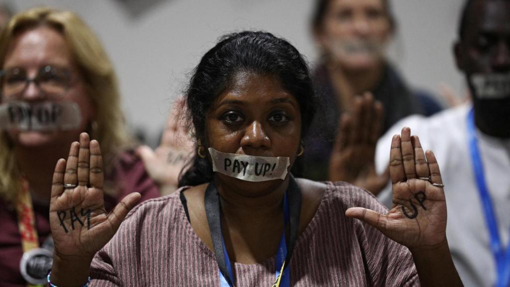 Una activista durante una protesta en la COP29 con una mordaza que reza pagad.