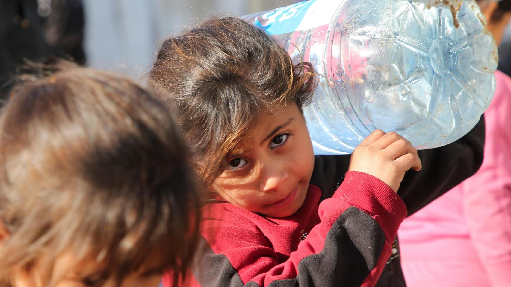 Una niña palestina portea garrafas de agua en un refugio de Gaza.