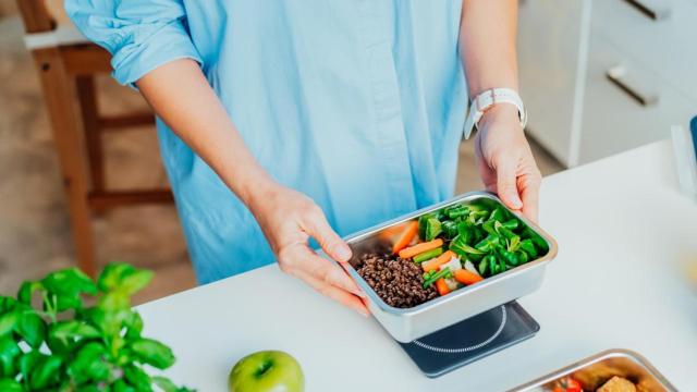 Mujer con un tupper con comida en la cocina.