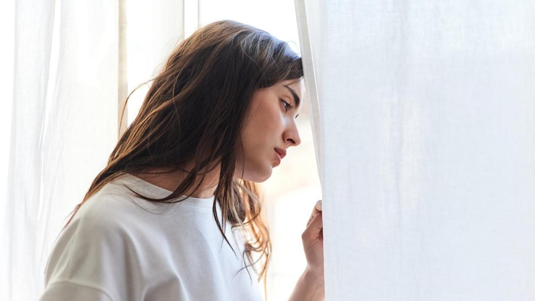 Mujer mirando por la ventana con aspecto triste.