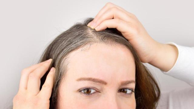 Mujer buscándose canas frente al espejo.