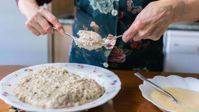 Una mujer rebozando croquetas utilizando dos cucharas de cocina.