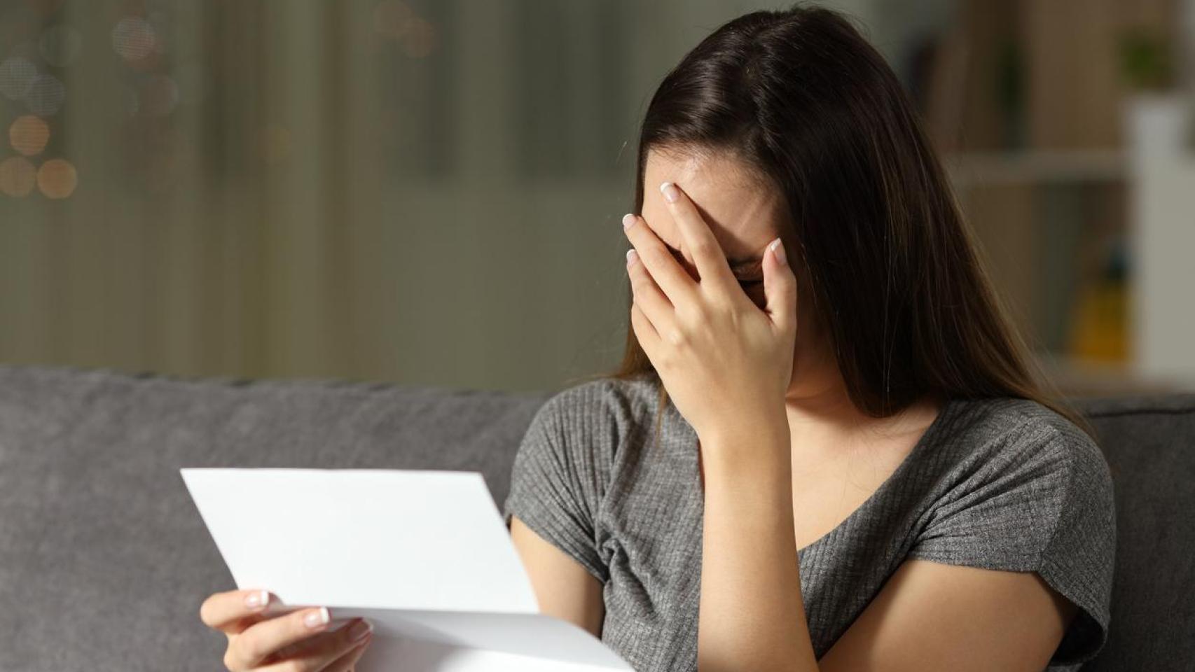 Fotografía de una mujer cubriéndose el rostro mientras lee una carta.