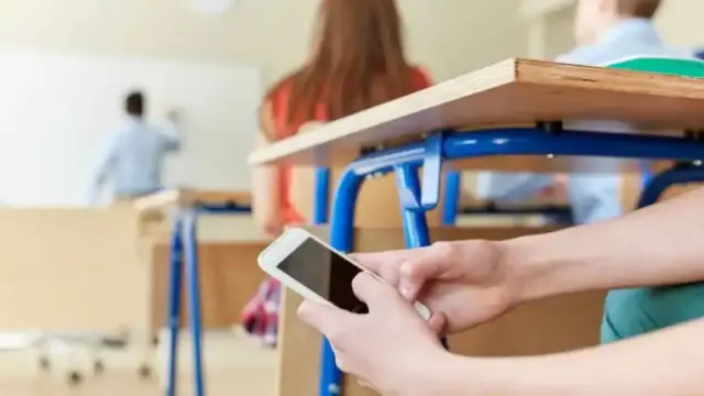 Un alumnos consultando su móvil dentro del aula.