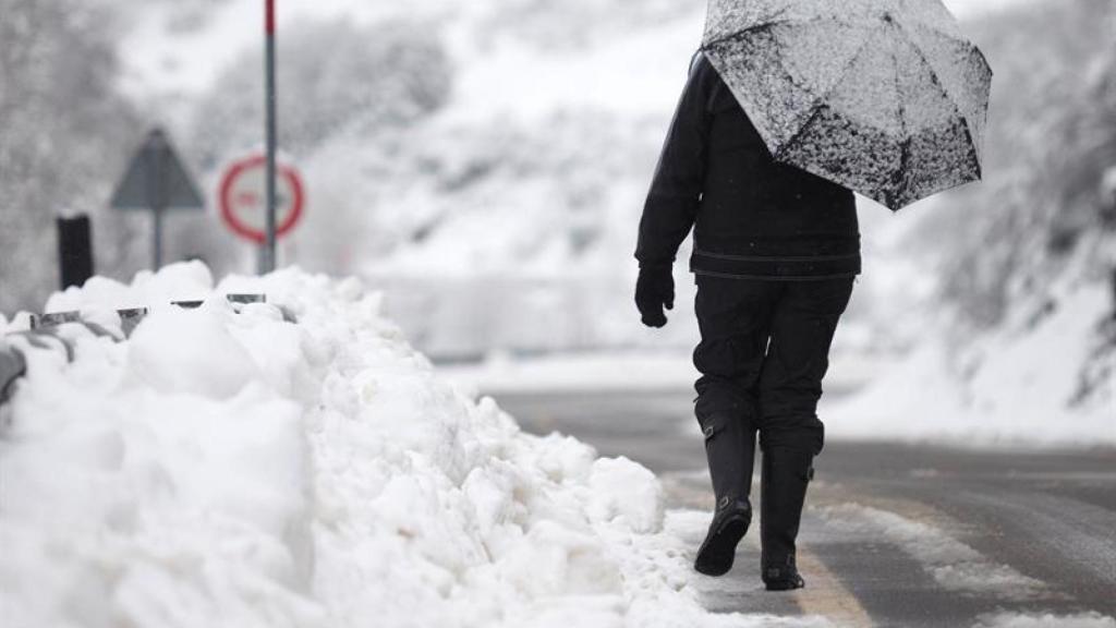 Una persona con paraguas andando por la nieve.