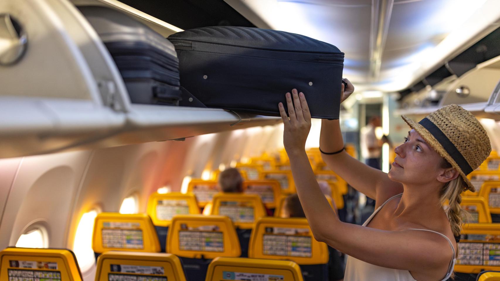 Una pasajera acomoda su maleta en el compartimento superior del avión.