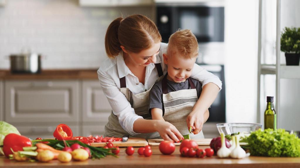 Una mujer cocina verduras con un niño