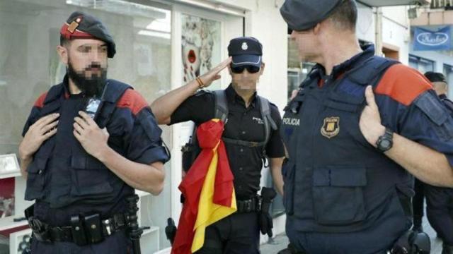 Un agente de la Policía Nacional, que porta una bandera de España, saluda a dos agentes de los Mossos.