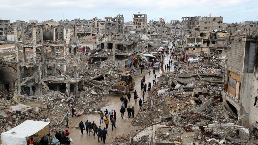 Un grupo de palestinos caminan entre el barro y los escombros de edificios destruidos por Israel.