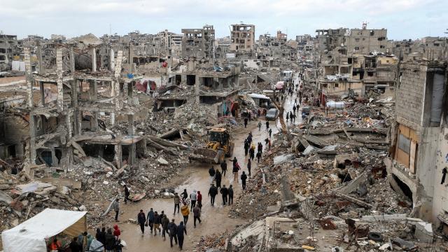 Un grupo de palestinos caminan entre el barro y los escombros de edificios destruidos por Israel.