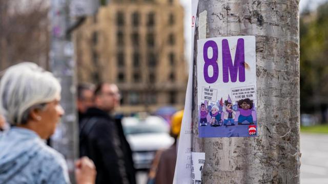 Una pegatina del 8M, por el Día Internacional de la Mujer, en un árbol de un concurrido paso de peatones de Madrid.