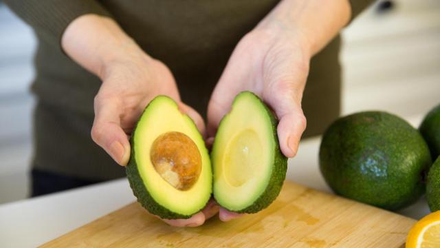 Unas manos sostienen un aguacate partido por la mitad.