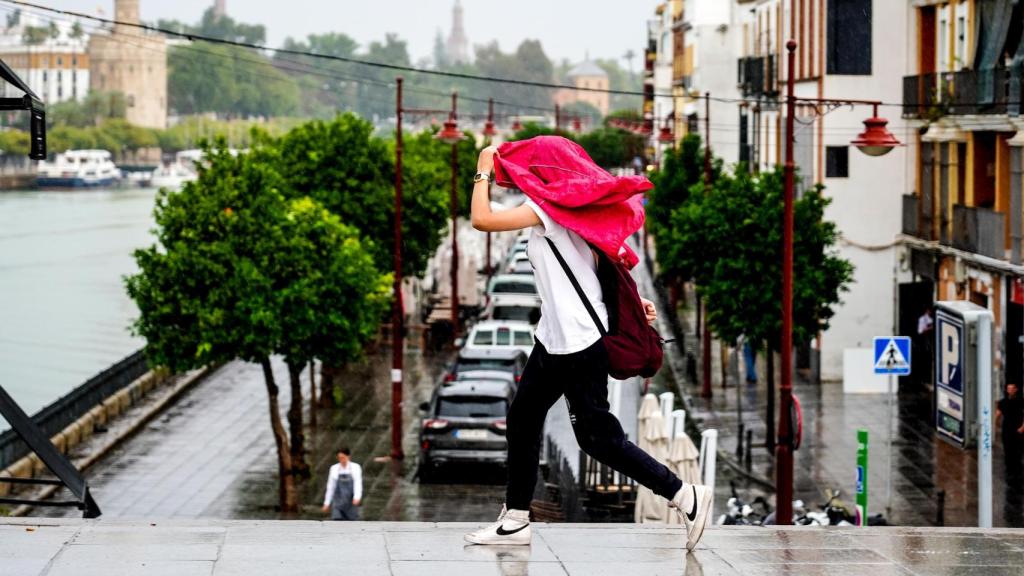 Una mujer se protege de la lluvia en Triana.