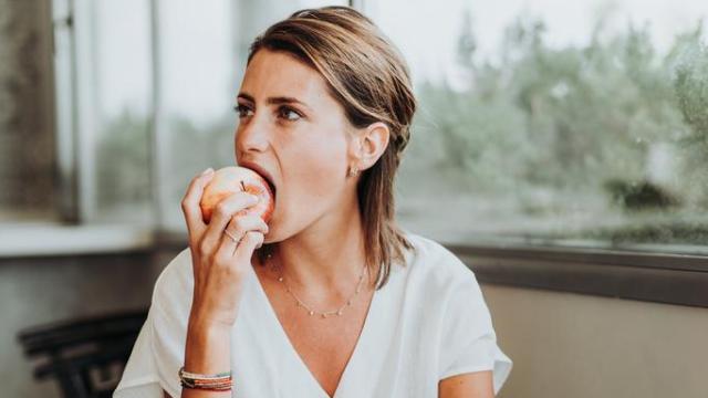 Mujer comiendo una manzana junto a una ventana.