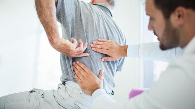 Un médico palpando la espalda de su paciente.