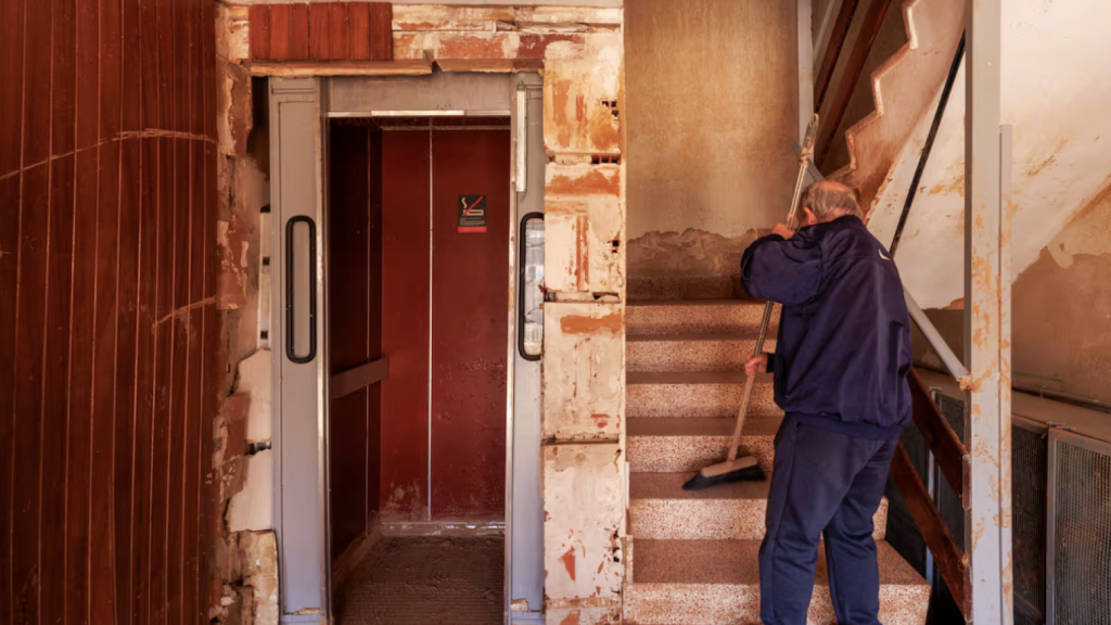 Un vecino de Paiporta barre las escaleras del portal de su edificio afectado por la dana. Villar Lopez / Efe