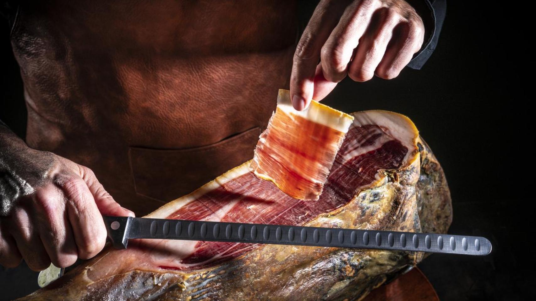 Imagen de archivo de una persona cortando jamón.