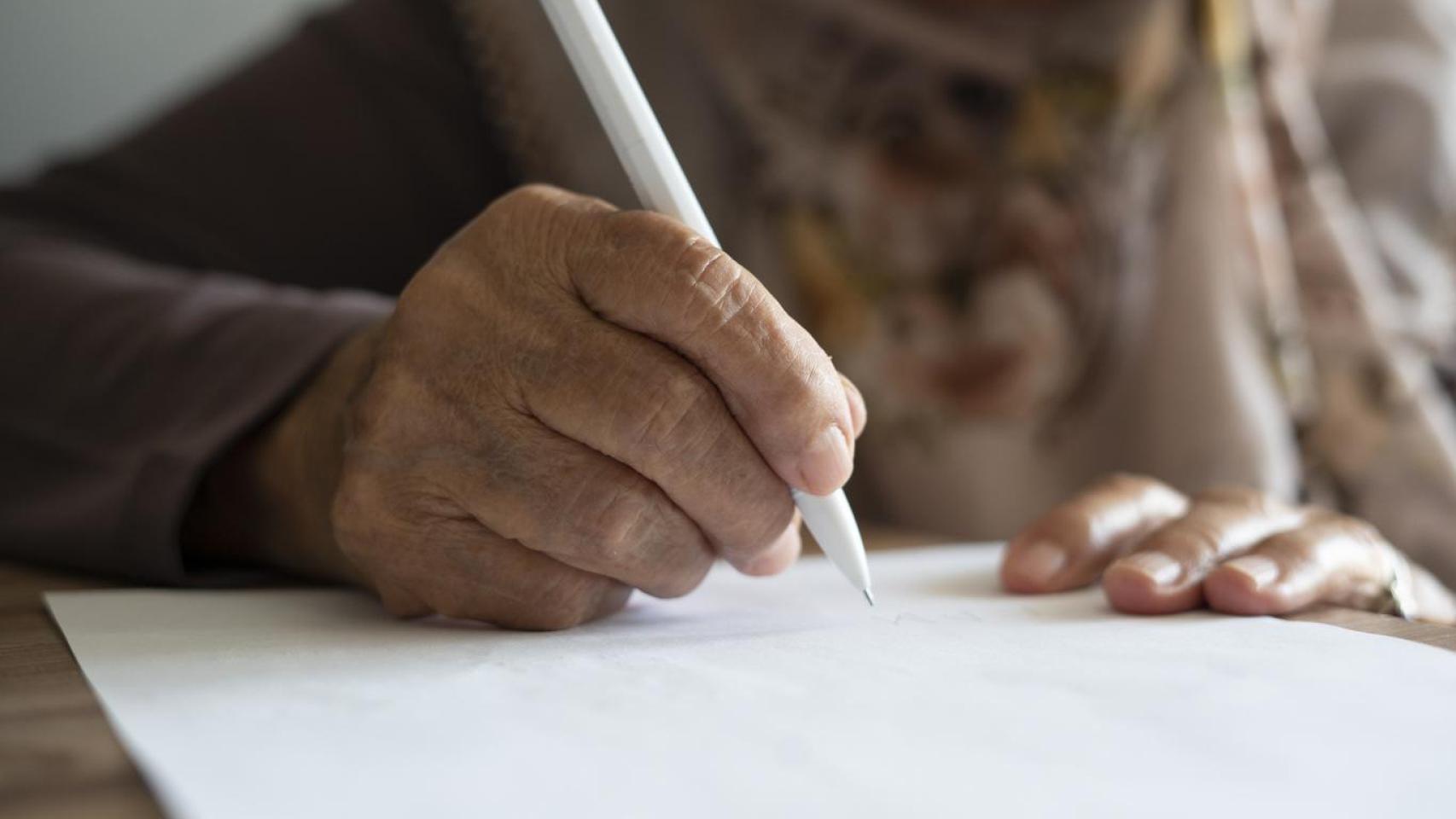 Mujer mayor escribiendo con bolígrafo.