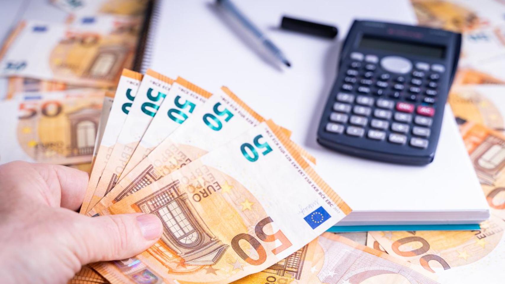 Varios billetes de 50 euros junto a una calculadora y un cuaderno.
