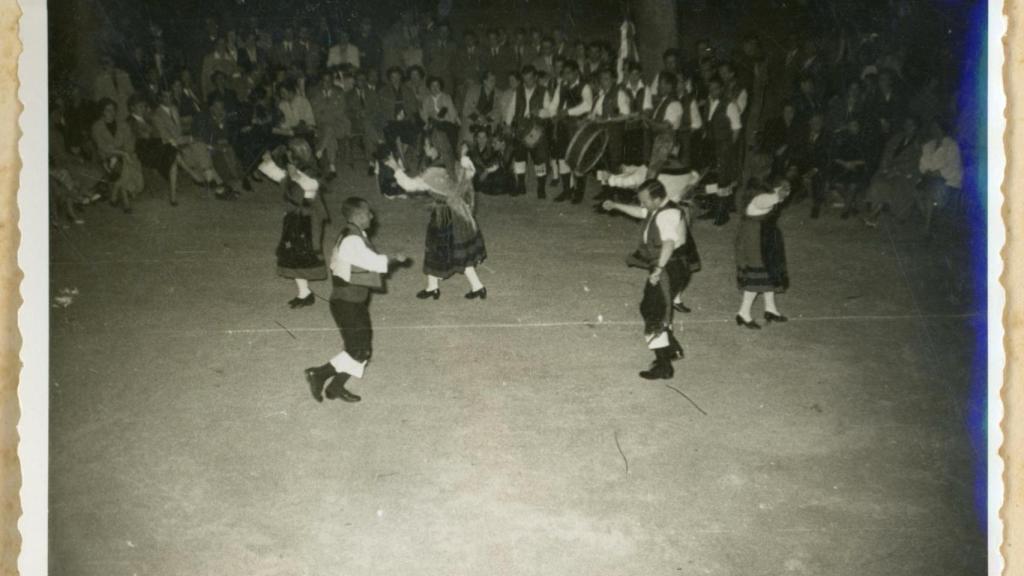 Hombres y mujeres bailando Muiñeira en una plaza.