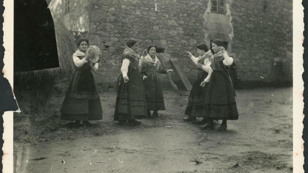 Cinco mujeres cantando y tocando la pandereta frente a una casa.