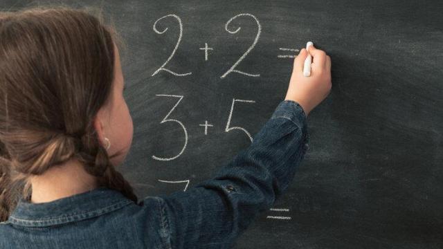 Una niña realizando una suma en la pizarra de clase.
