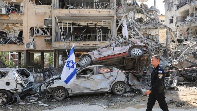 Un agente de policía israelí pasa junto a vehículos dañados en el lugar del impacto de un misil iraní contra Israel, en Ramat Gan, Israel.