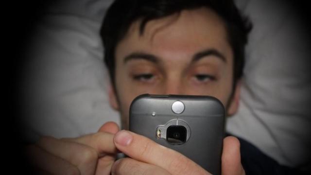 Un joven mira el móvil acostado en una cama.