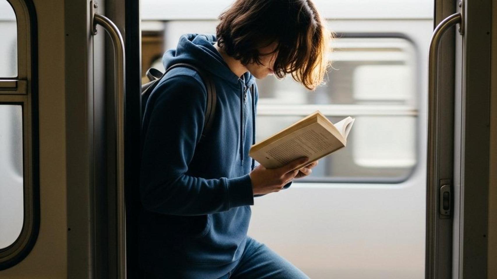Un joven leyendo un libro en un tren.