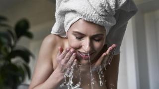 Mujer lavándose la cara con agua del grifo.