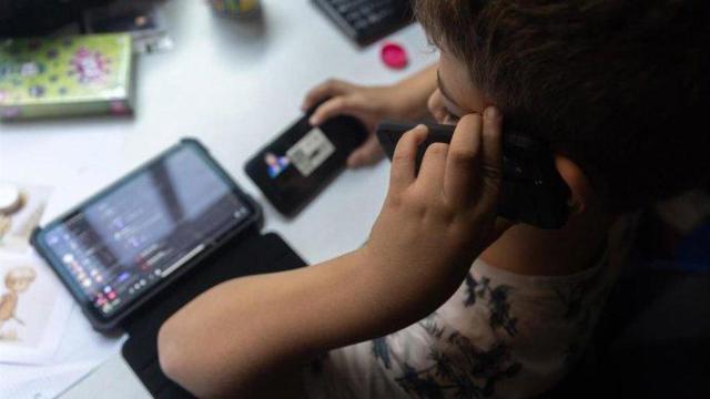 Un niño usa a la vez varios dispositivos electrónicos.