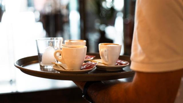 Una bandeja con cafés y sostenida por un camarero.