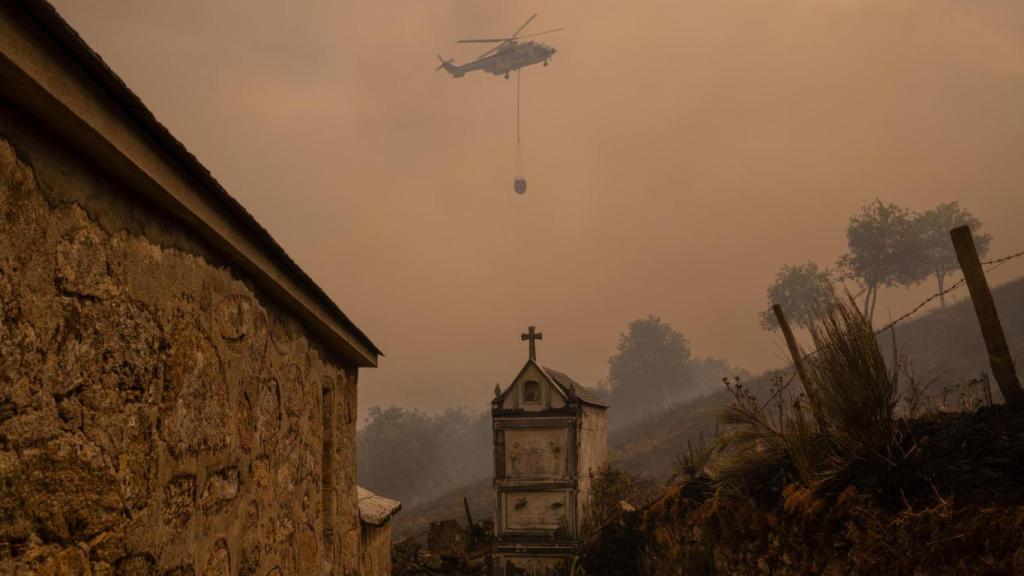 Un helicóptero de control de incendios sobrevuela el cementerio de Vilar durante un incendio forestal.